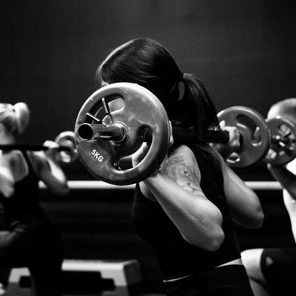 Three women squating with barbells in a studio