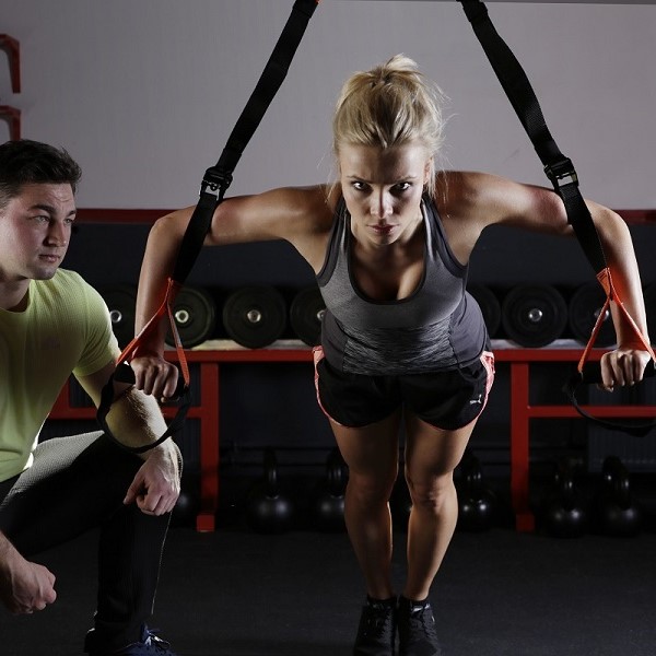 Woman doing a push up using suspension training and a personal trainer kneeling and supervising 